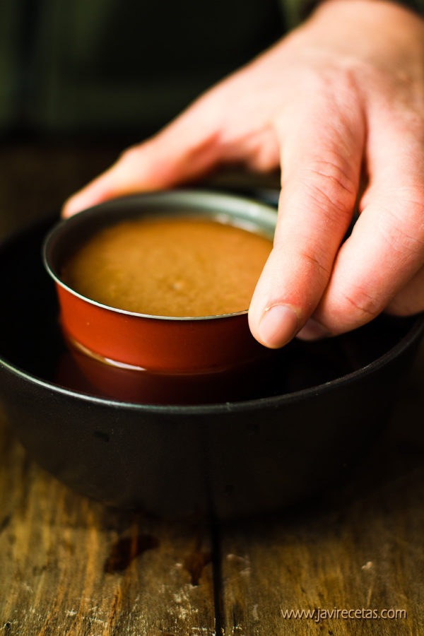 Mano sujetando molde del flan y metiéndolo en un cuenco de agua caliente